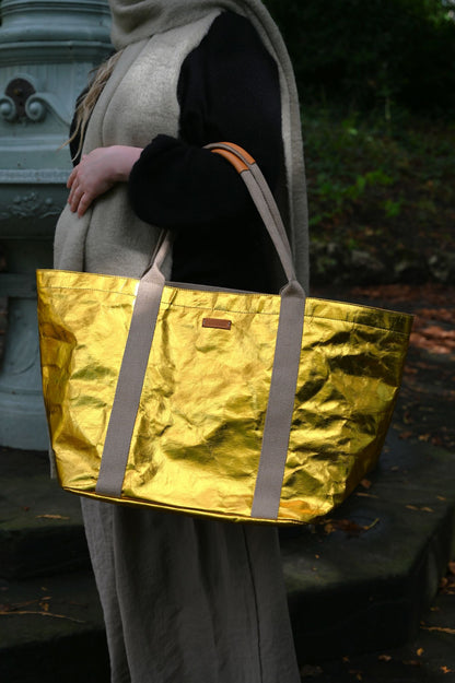 Person holding a gold metallic tote bag outdoors
