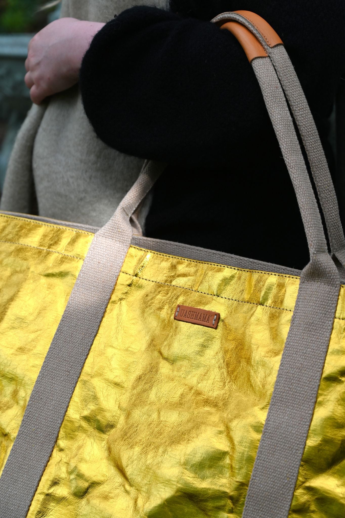 Gold tote bag held by a person wearing a black coat.