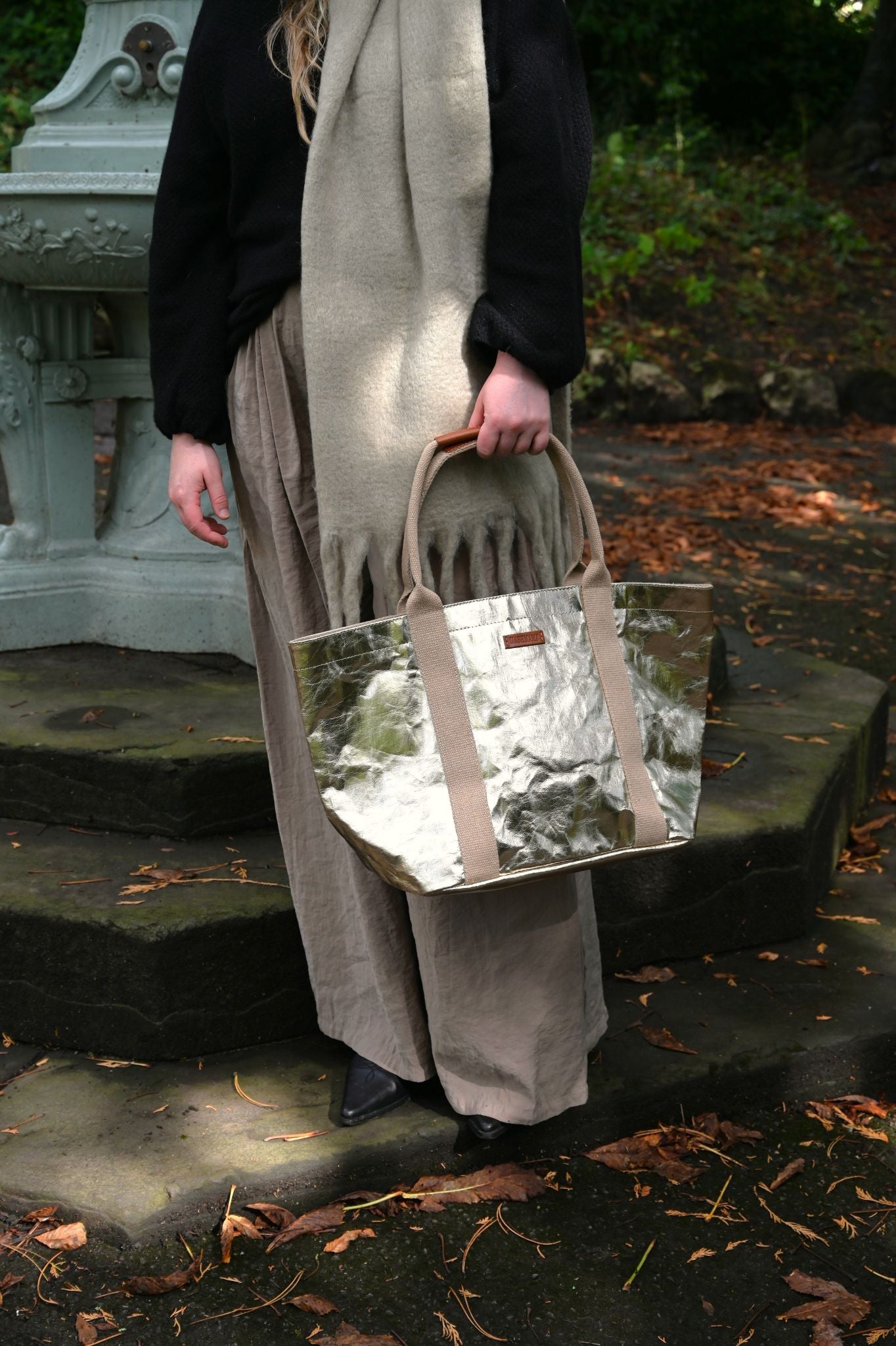 Person holding a pale gold tote bag outdoors on stone steps