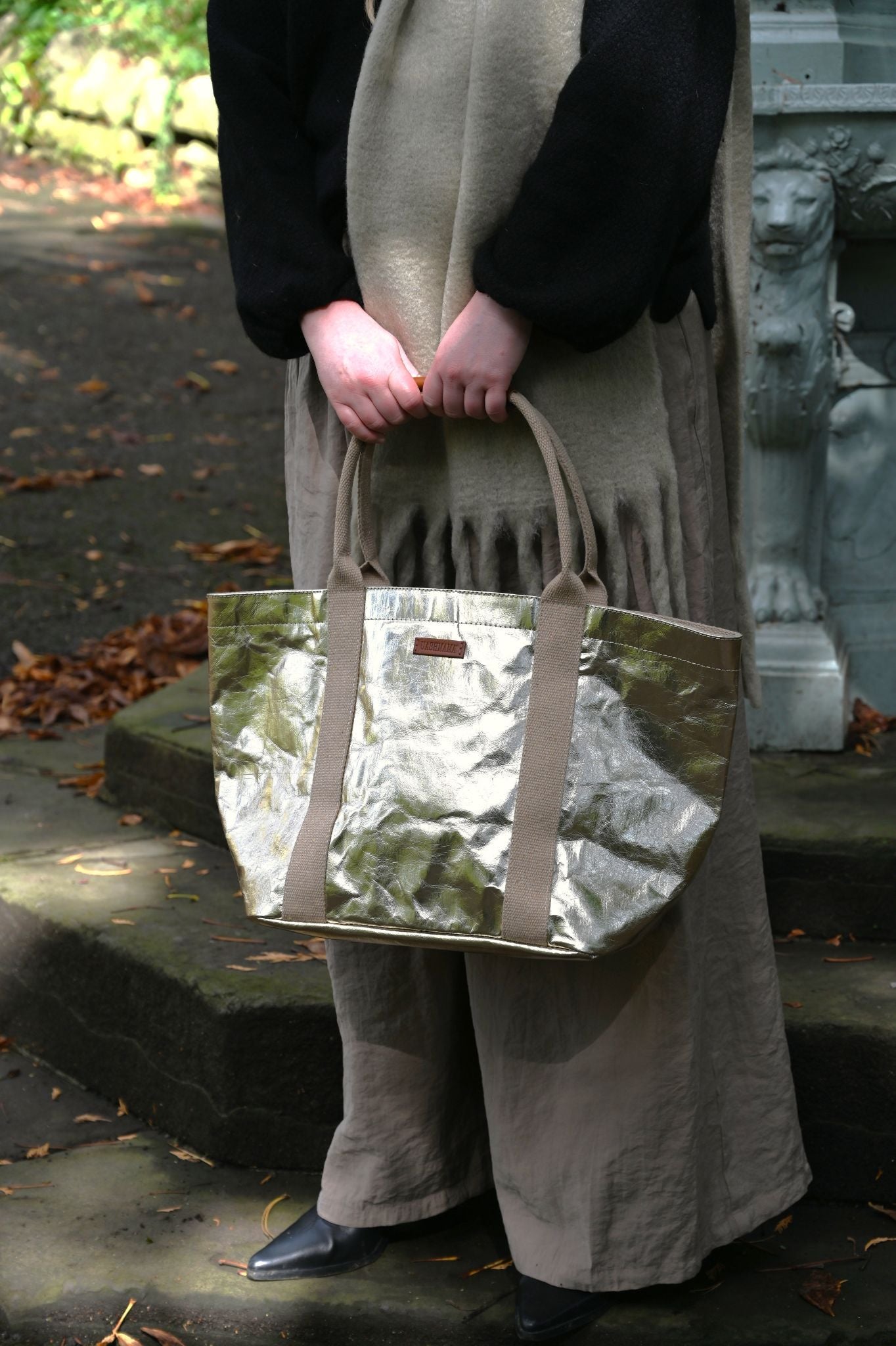 Person holding a pale gold tote bag outdoors on stone steps.