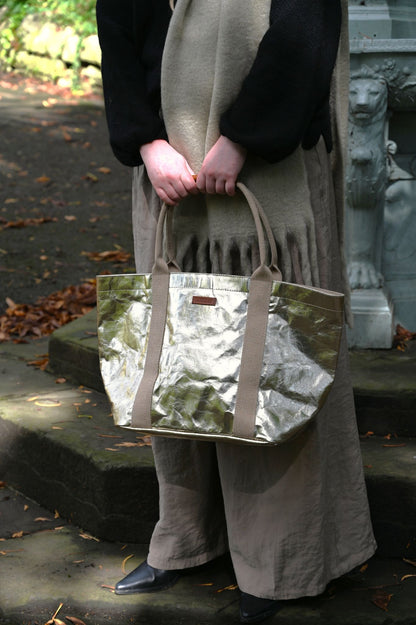 Person holding a pale gold tote bag outdoors on stone steps.