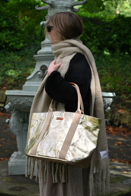 Person holding a pale gold tote bag with a scarf in an outdoor setting