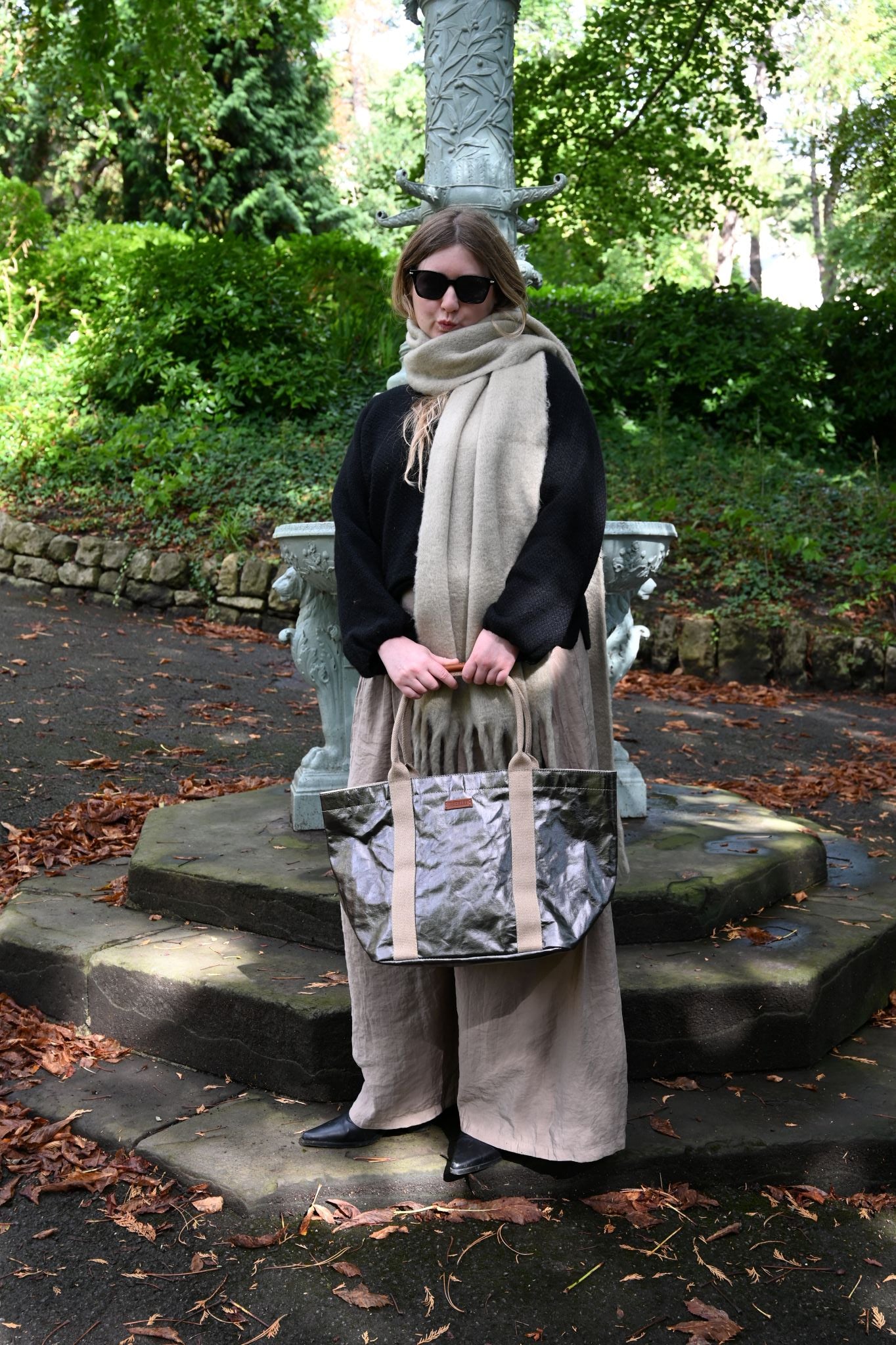 Person holding a small gunmetal tote bag outdoors with greenery in the background