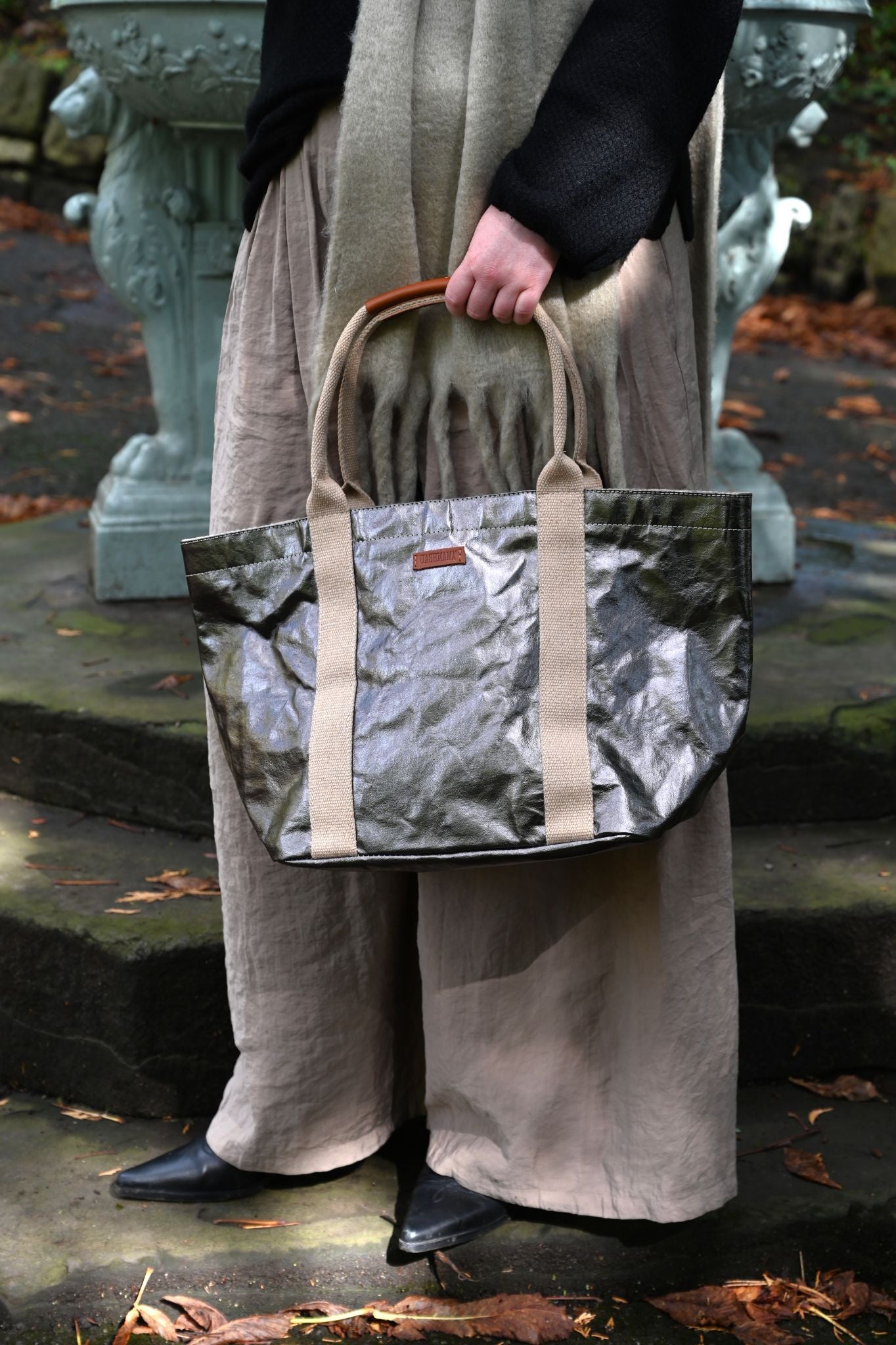 Person holding a small gunmetal tote bag outdoors with a statue in the background