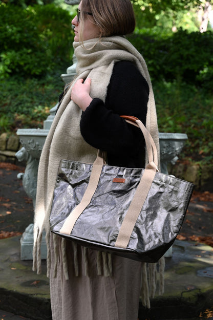 Person holding a small gunmetal tote bag, in the outdoors.