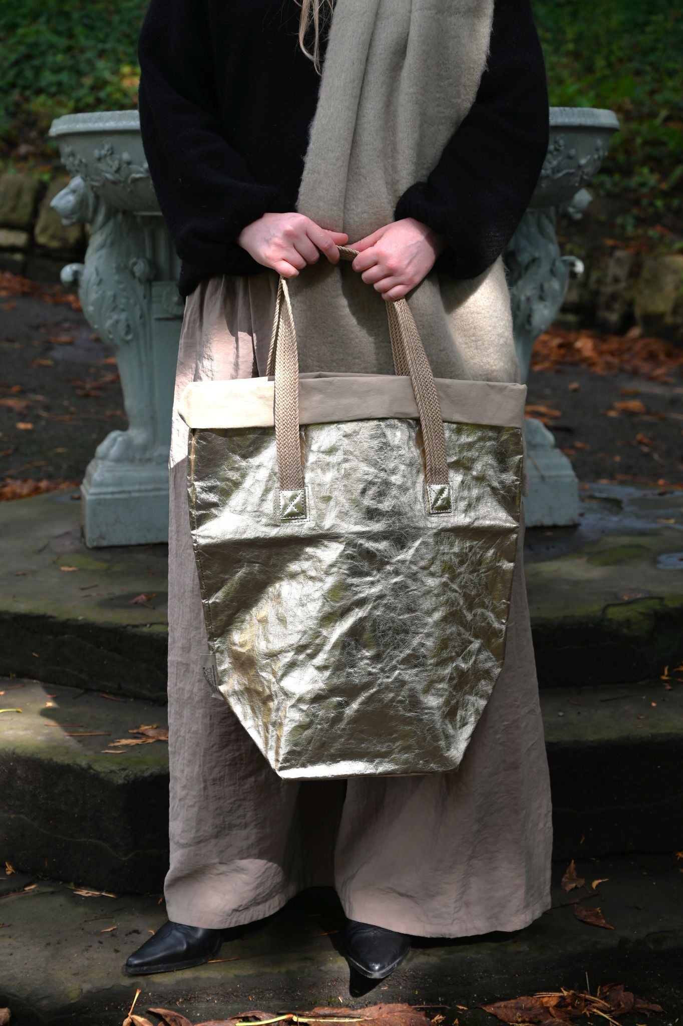 Person holding a large metallic pale gold bag outdoors on stone steps.