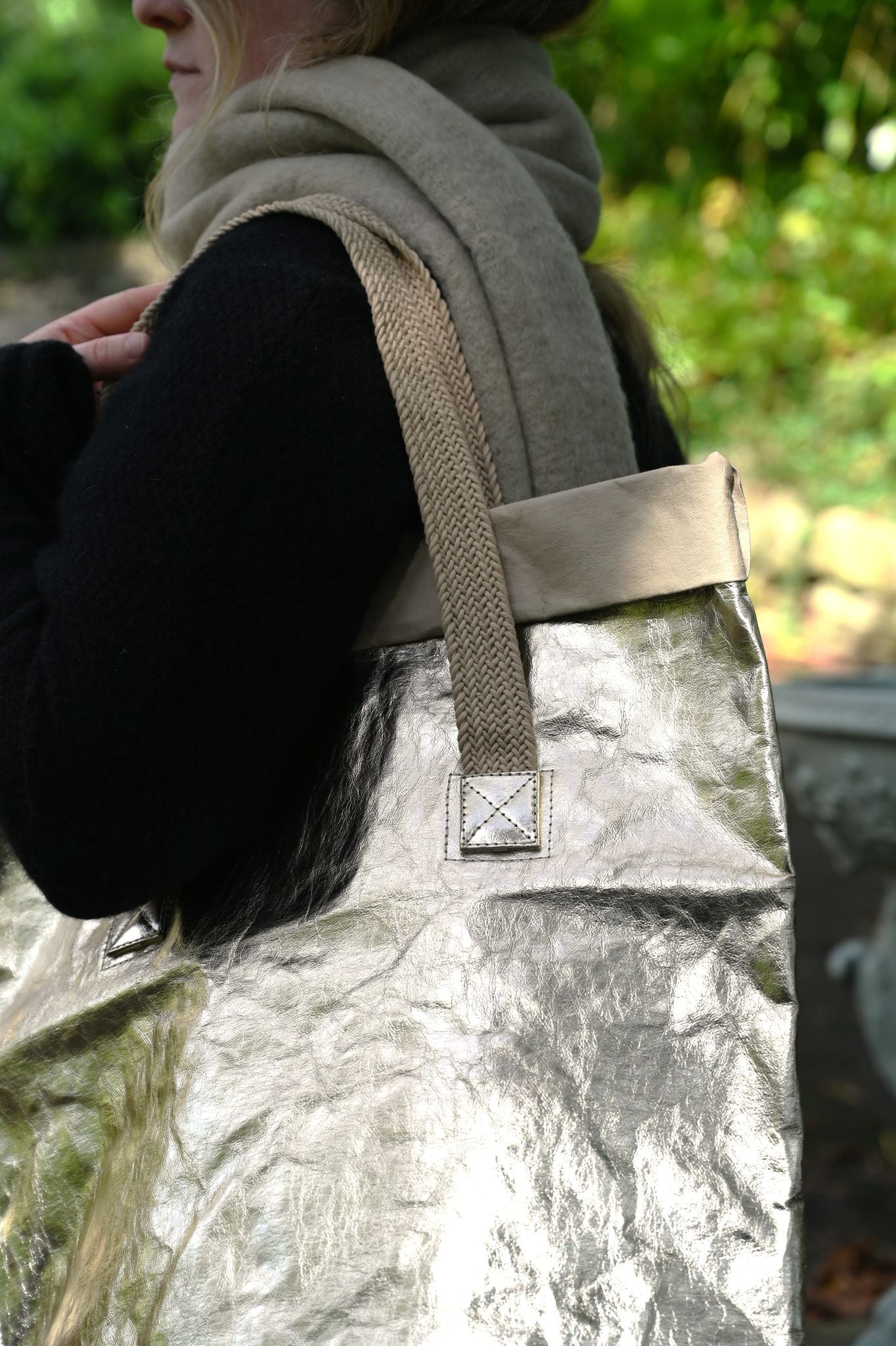 Person holding a metallic pale gold bag with a strap in an outdoor setting
