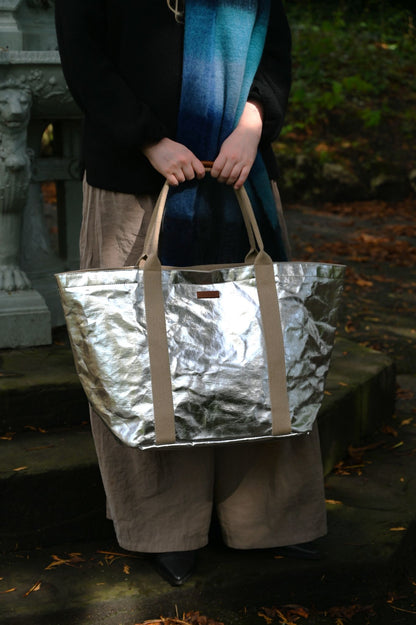 Person holding a metallic large silver tote bag outdoors