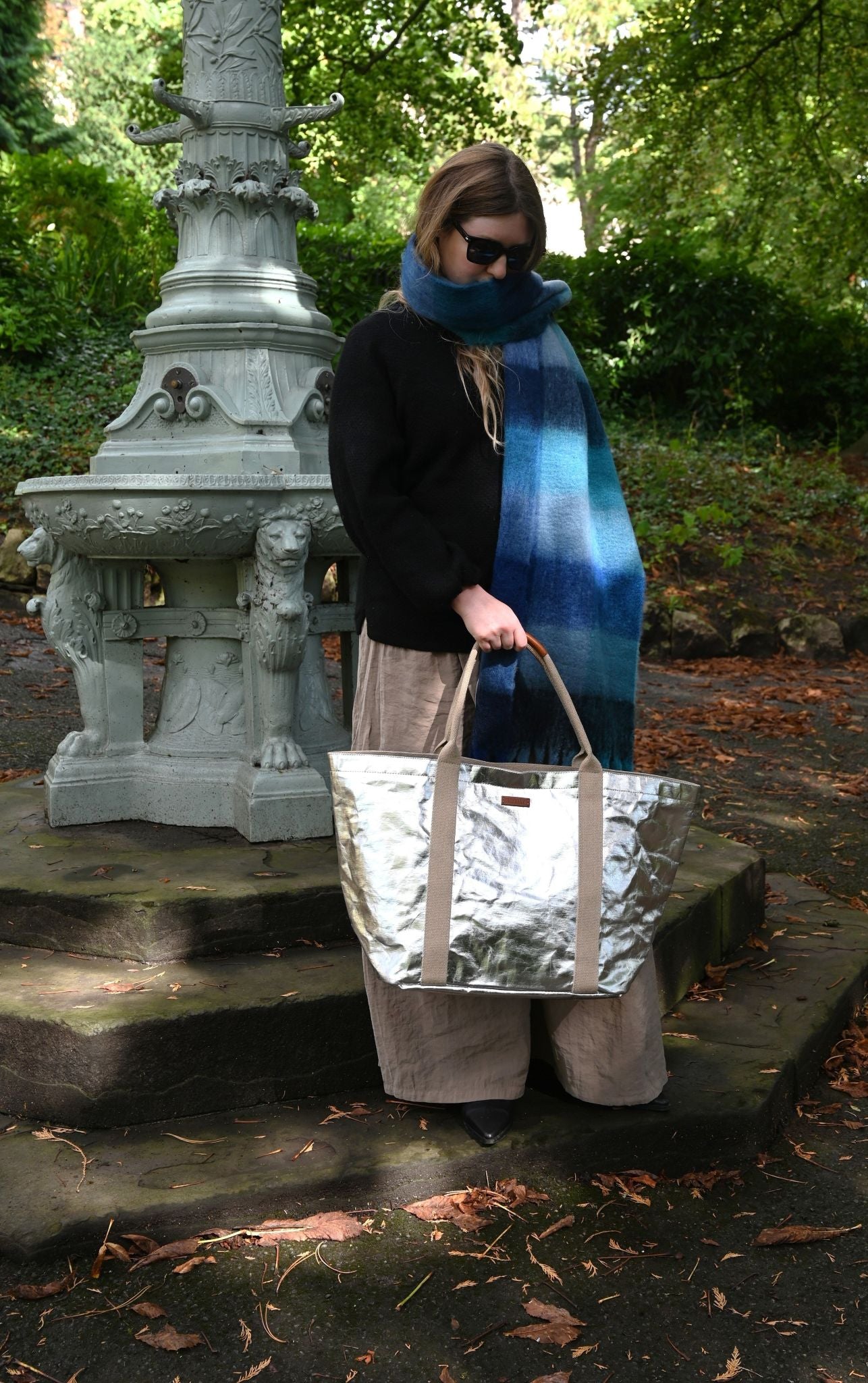 Person holding a silver bag in an outdoor setting with greenery