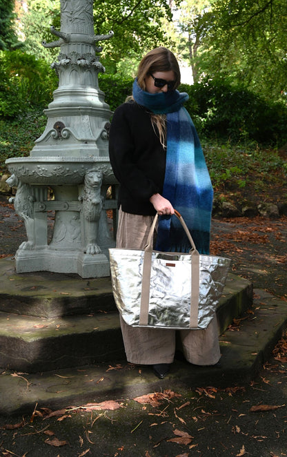 Person holding a silver bag in an outdoor setting with greenery