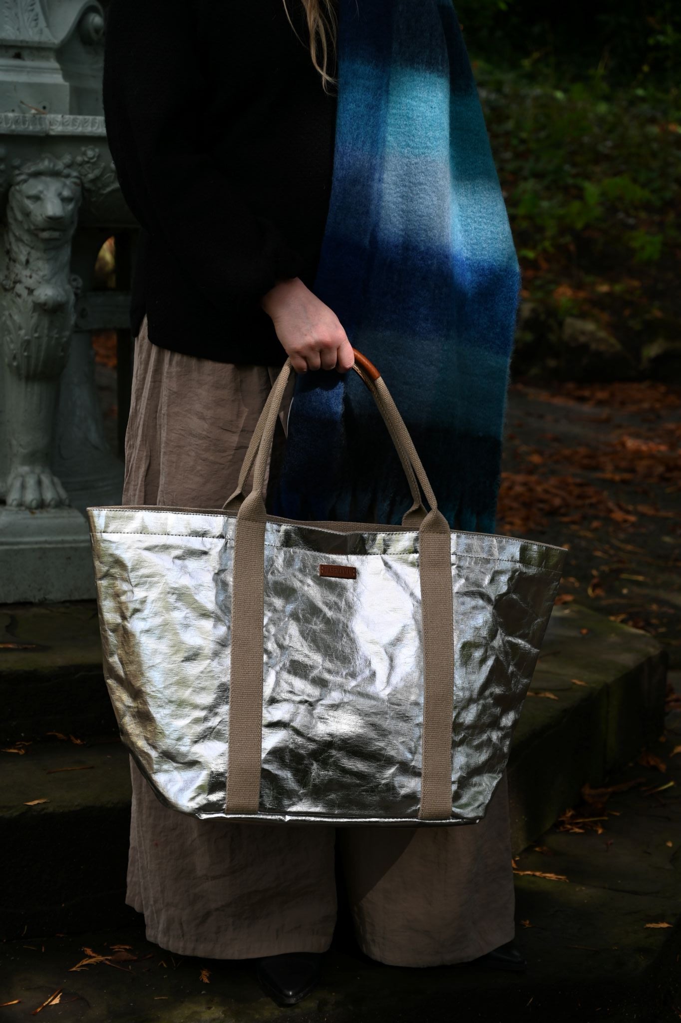 Person holding a metallic large silver tote bag with a dark background