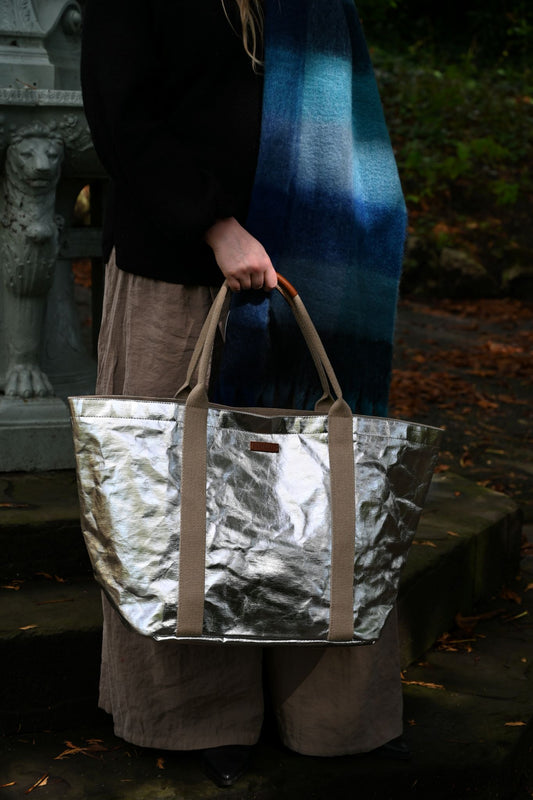 Person holding a metallic large silver tote bag with a dark background