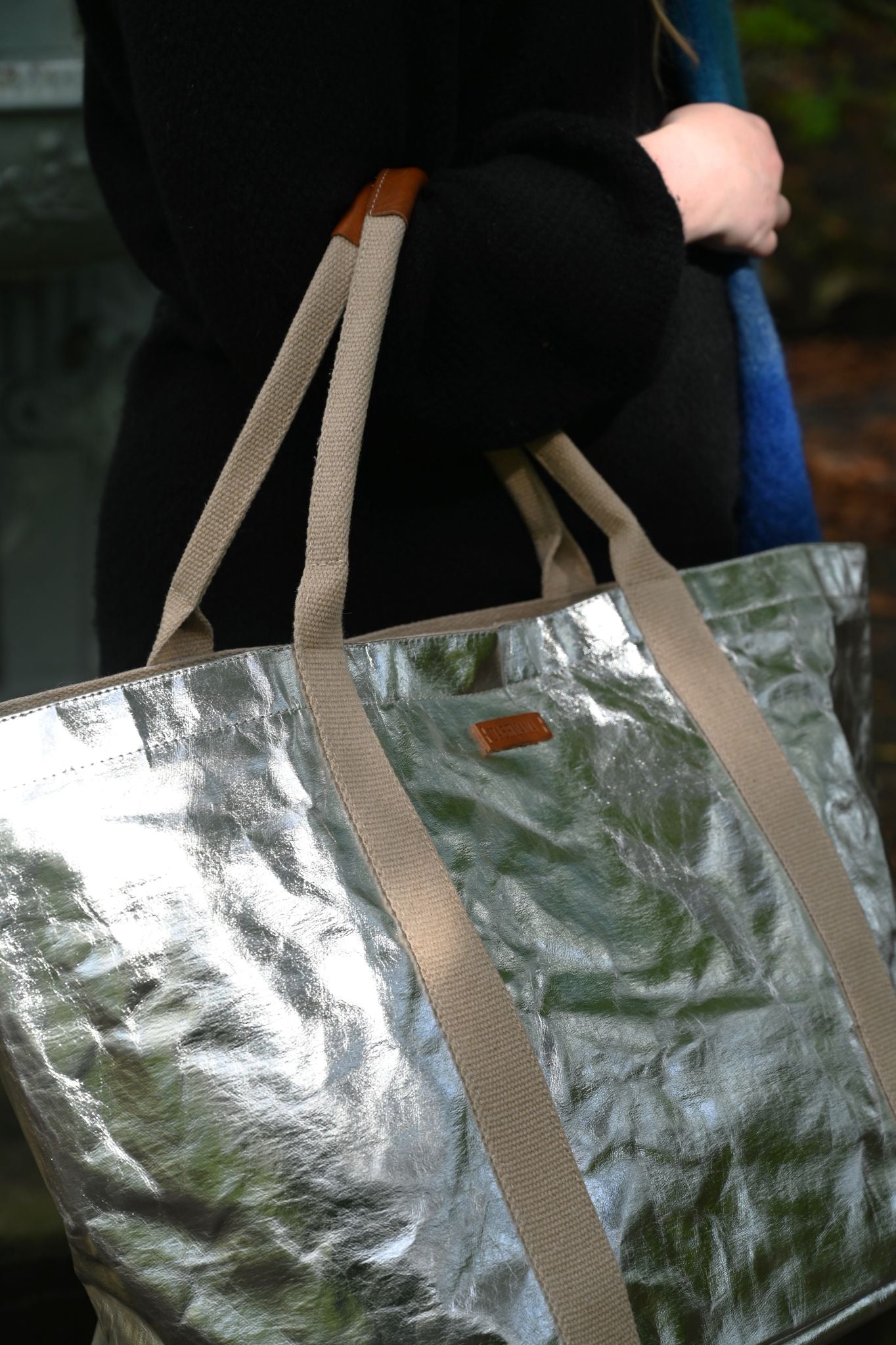 Person holding a large silver tote bag with beige straps.