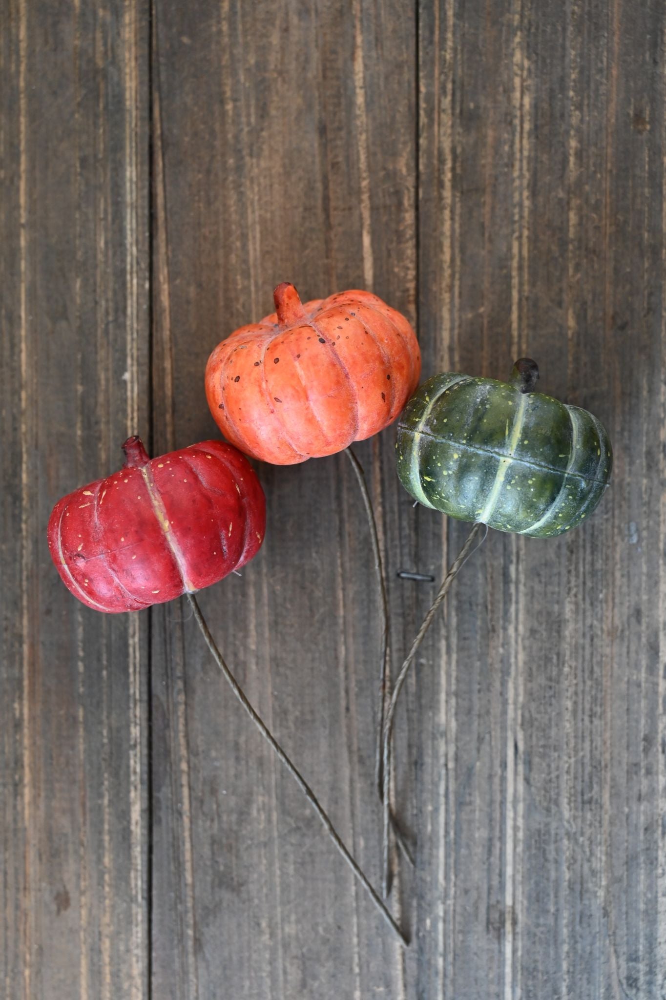 Three decorative pumpkins in red, orange, and green on a wooden surface