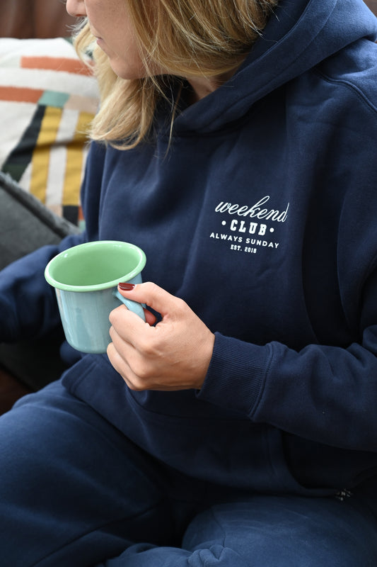 Person wearing a navy hoodie with weekend club text, holding a green cup.