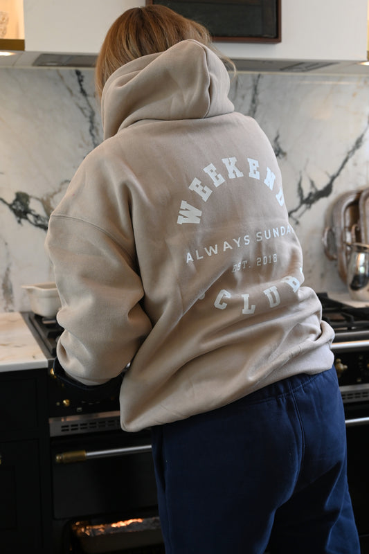 Person wearing a beige hoodie and navy joggers with weekend club text in a kitchen setting