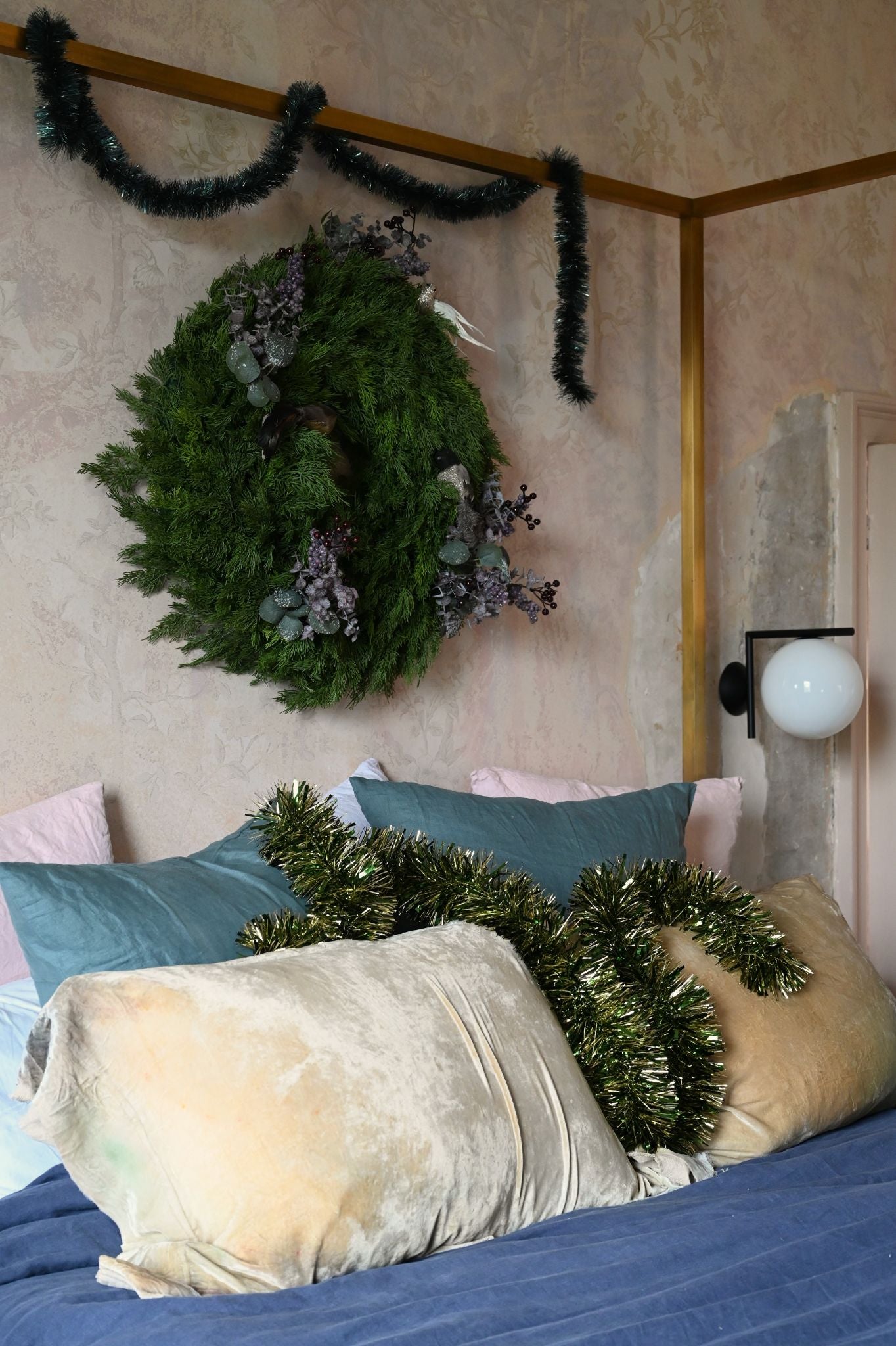 Large green Cyprus wreath on a textured wall and tinsel on pillows in a bedroom setting