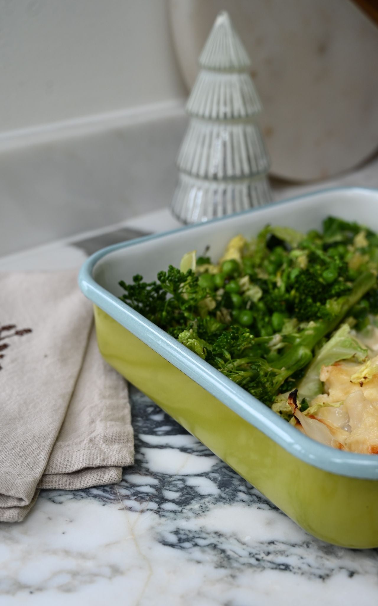 Green square enamel tray with food on a marble surface next to a decorative item.