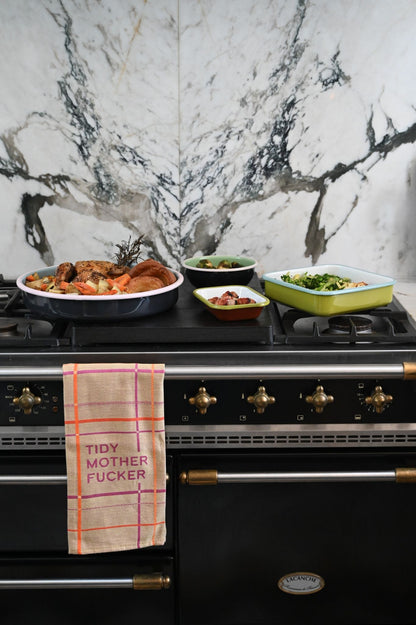 Black stove with Always Sunday enamel trays and a decorative tea towel on a marble wall background