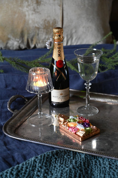 Decorative setting with a wine glass, christmas decoration and clear glass lamp t-light holder on a metal tray.