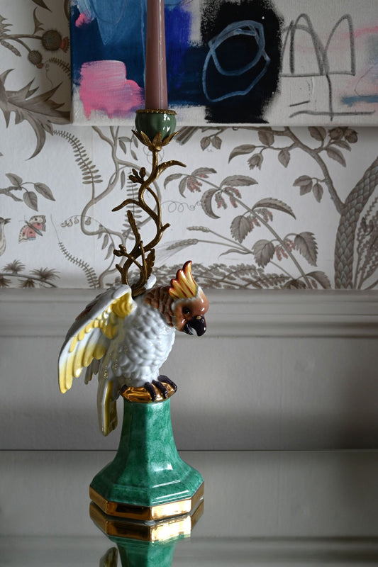 Decorative candle holder with blue parakeet design against a patterned wall.