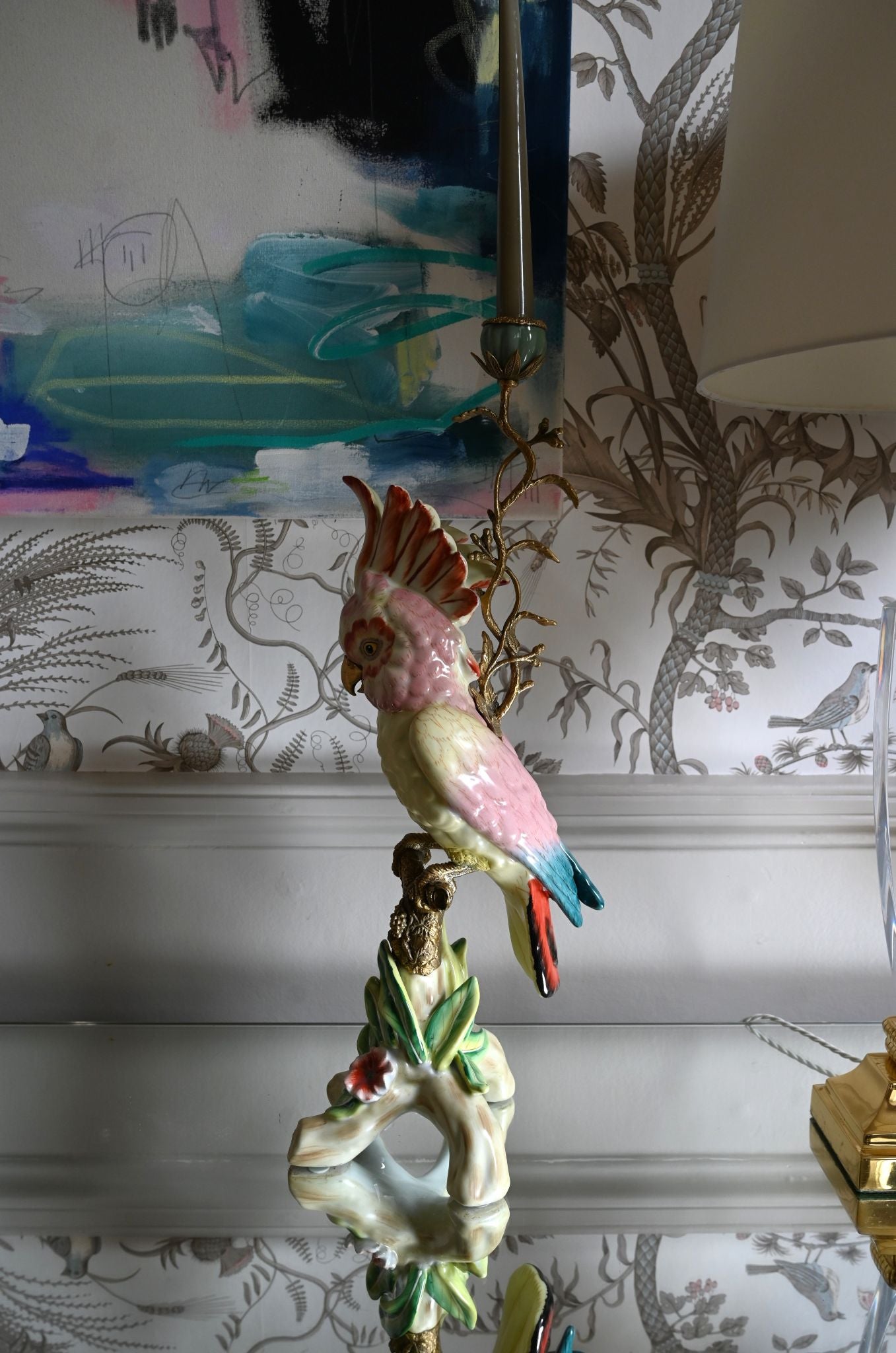 Decorative large pink parakeet ceramic candle holder on a table with a patterned wallpaper background