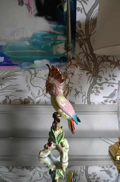 Decorative large pink parakeet ceramic candle holder on a table with a patterned wallpaper background