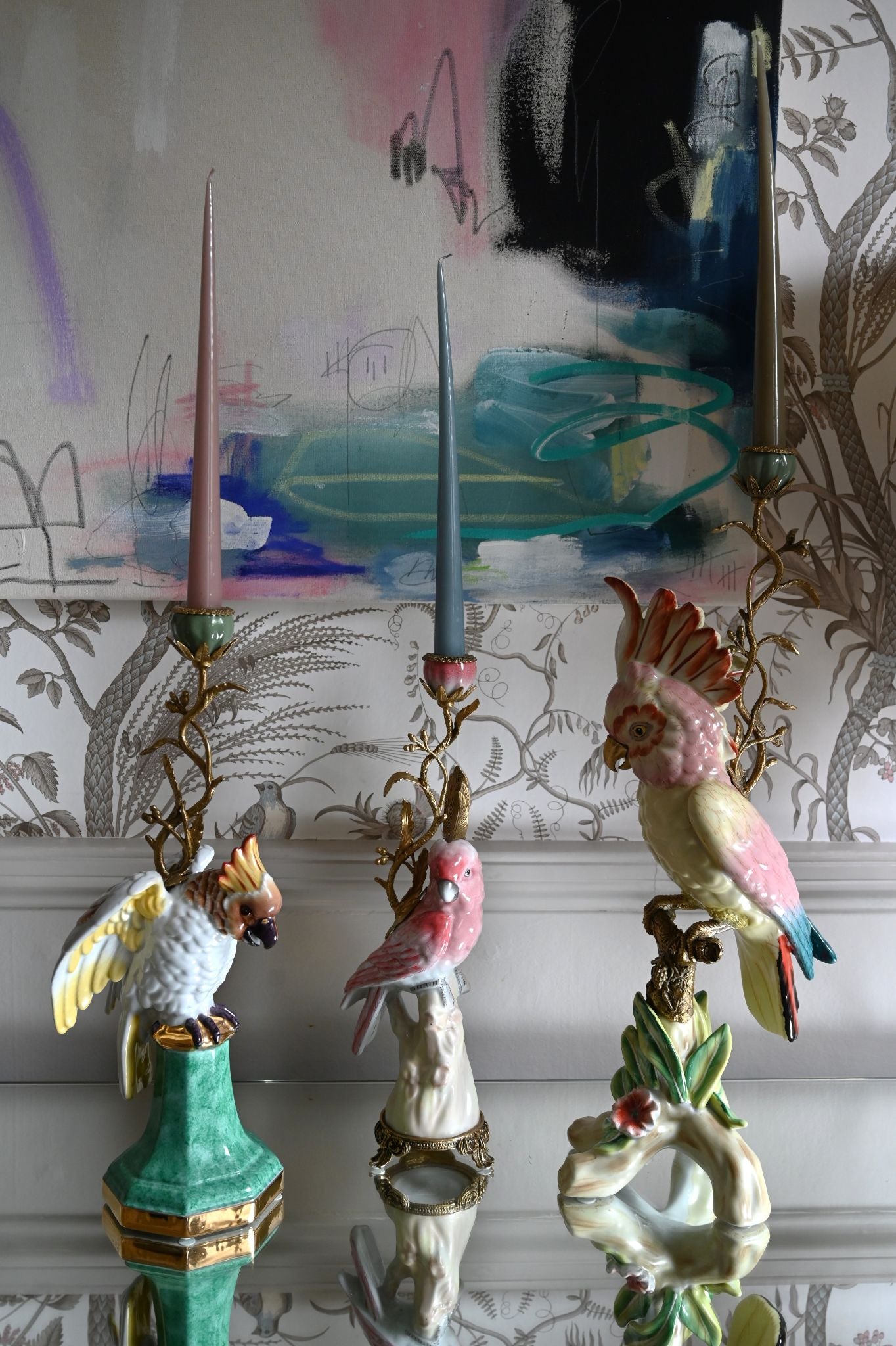 Decorative candle holders with parrot and parakeet designs against a colorful abstract wall.
