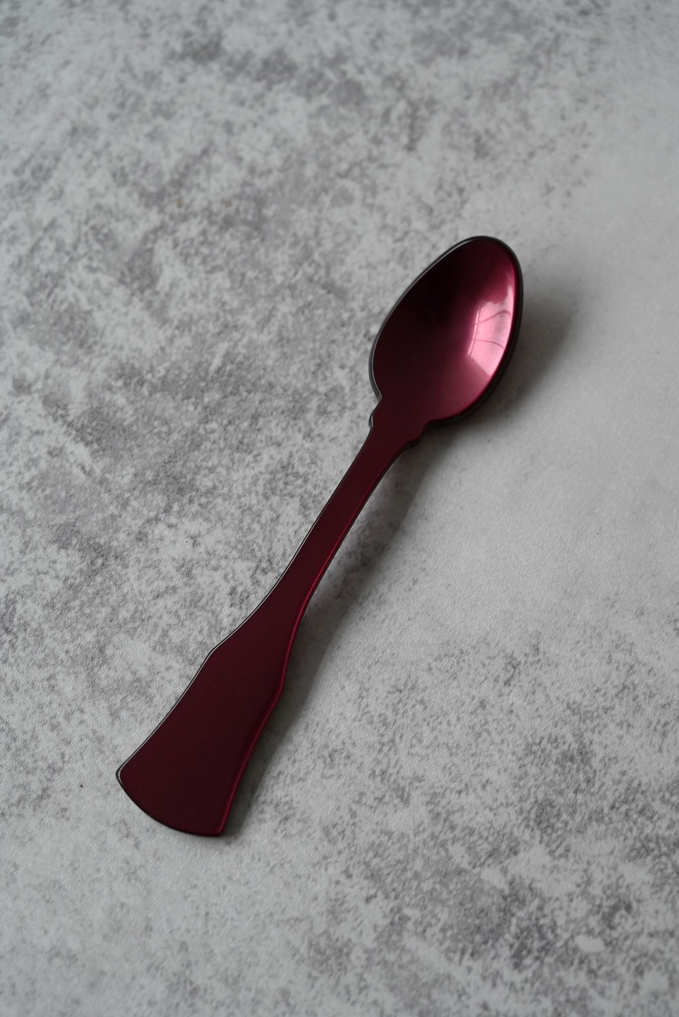 Six colourful shimmering acrylic demitasse spoons with flared handles on a grey surface.