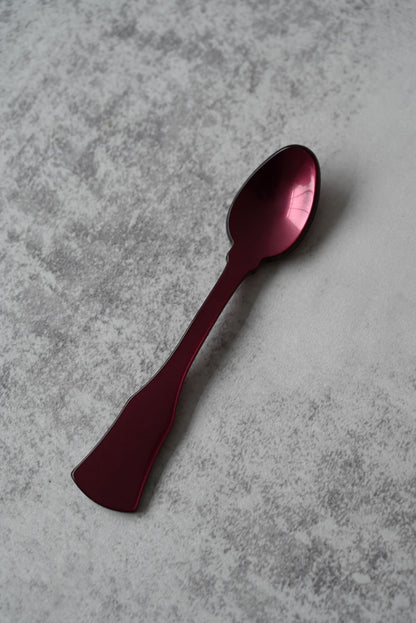Six colourful shimmering acrylic demitasse spoons with flared handles on a grey surface.