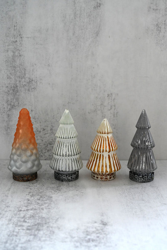 Four decorative glass Christmas trees with different designs and colors on a textured surface.