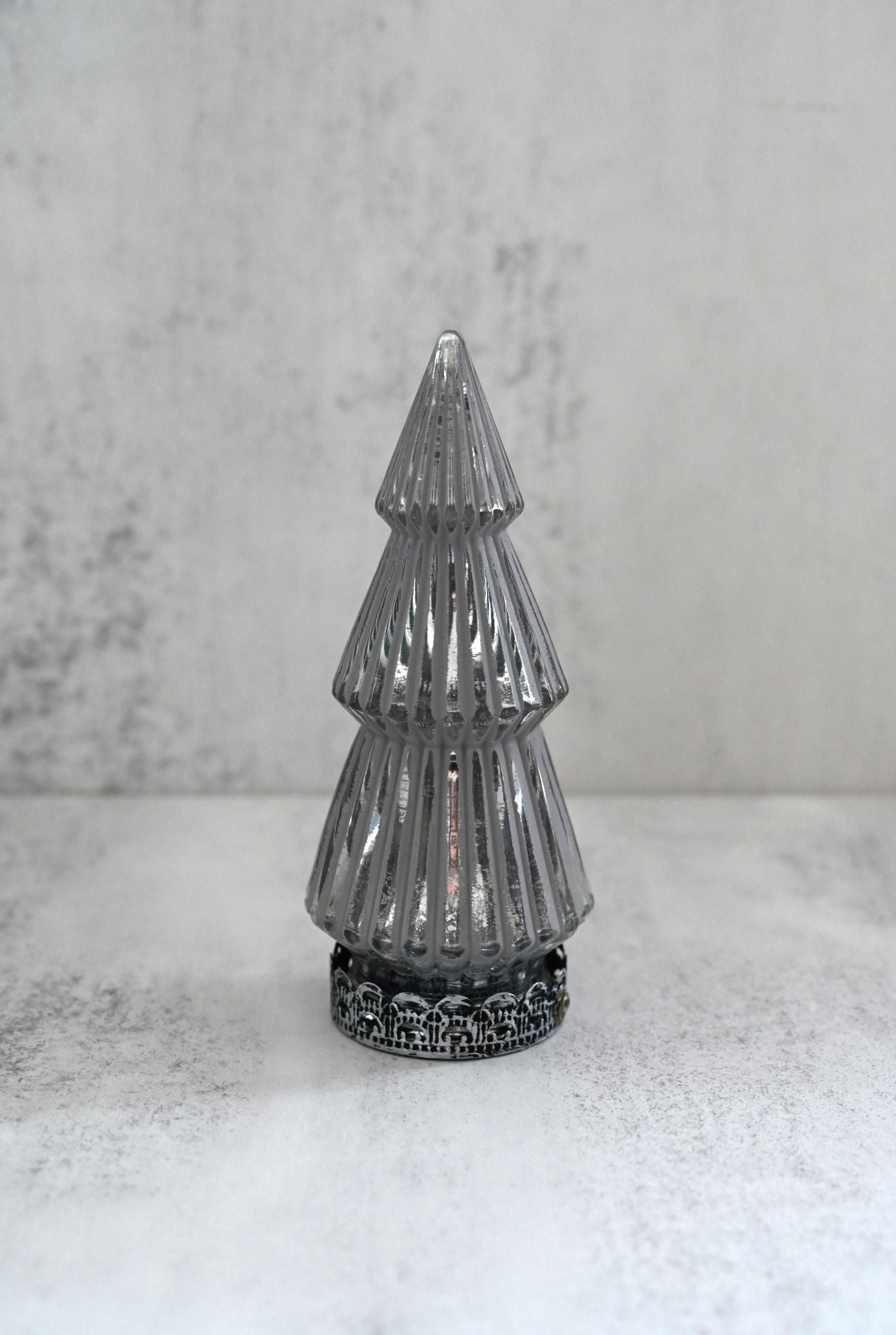Decorative silver Christmas tree on a white surface with a gray background