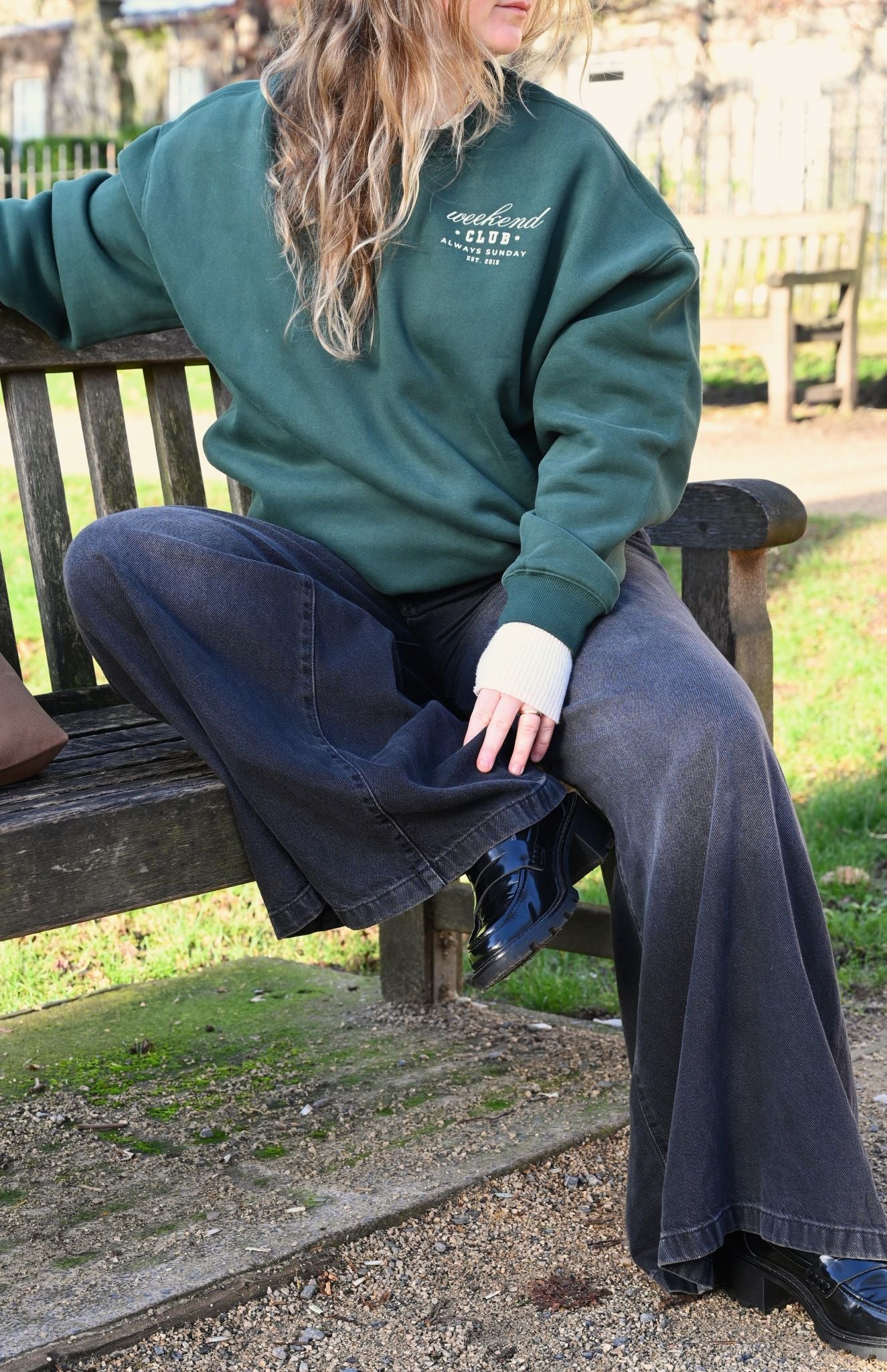 Person wearing a green sweatshirt with text, sitting on a bench outdoors.