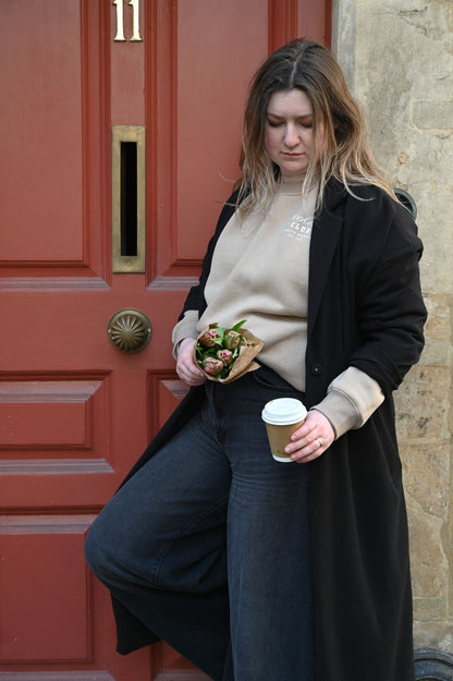 Woman holding a coffee cup and a sandwich in front of a red door.