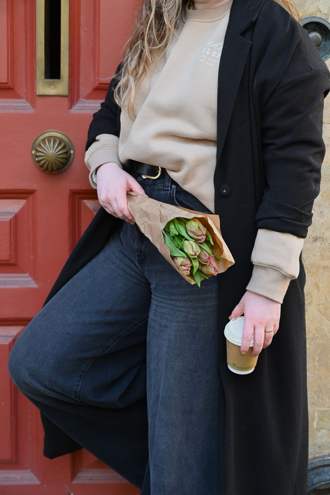 Person holding a sandwich and a coffee cup in front of a red door.