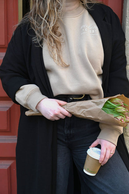 Person holding a coffee cup and a bouquet of tulips against a red door.