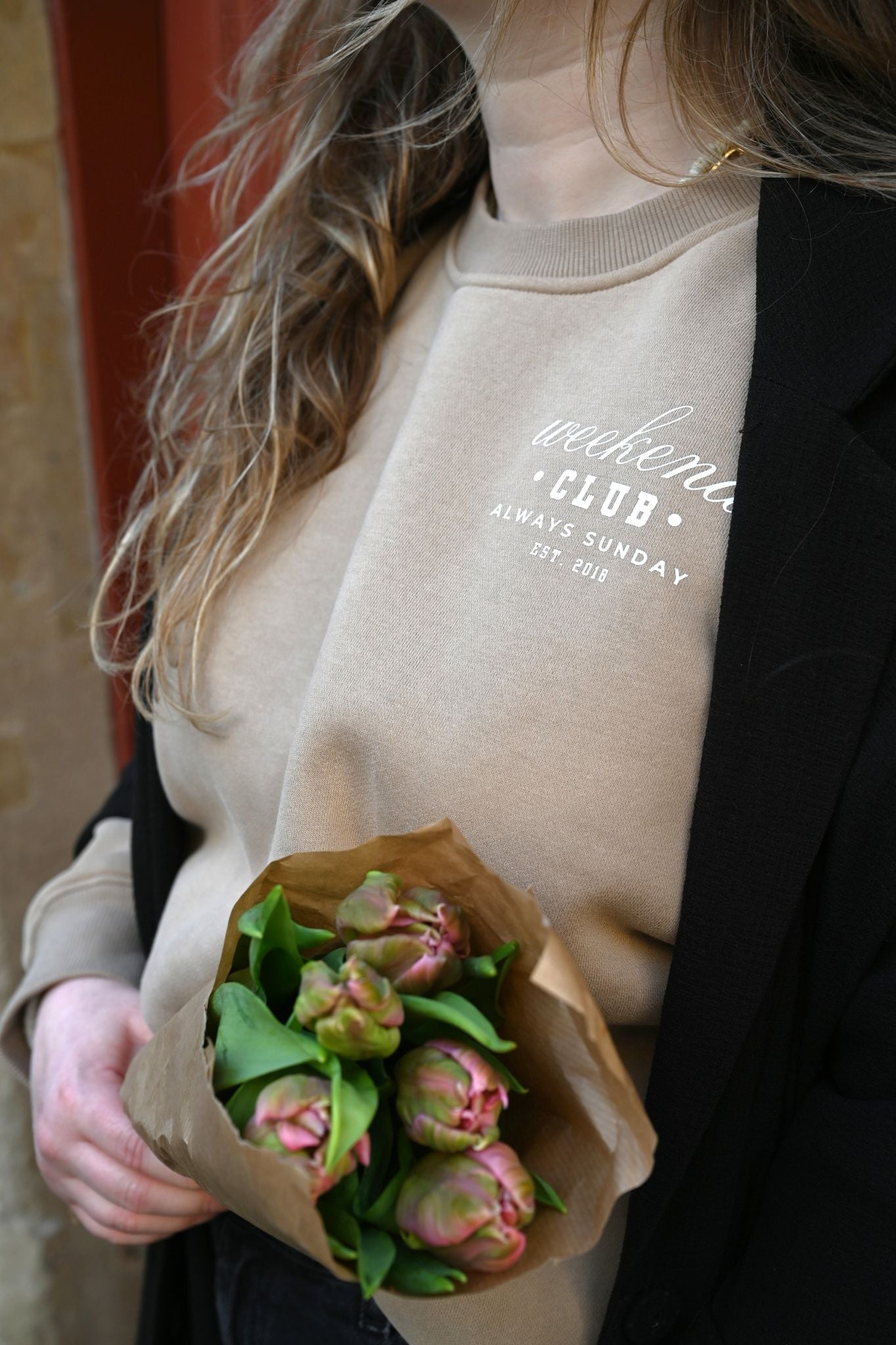 Person holding a bouquet of flowers wearing a beige sweater with text.