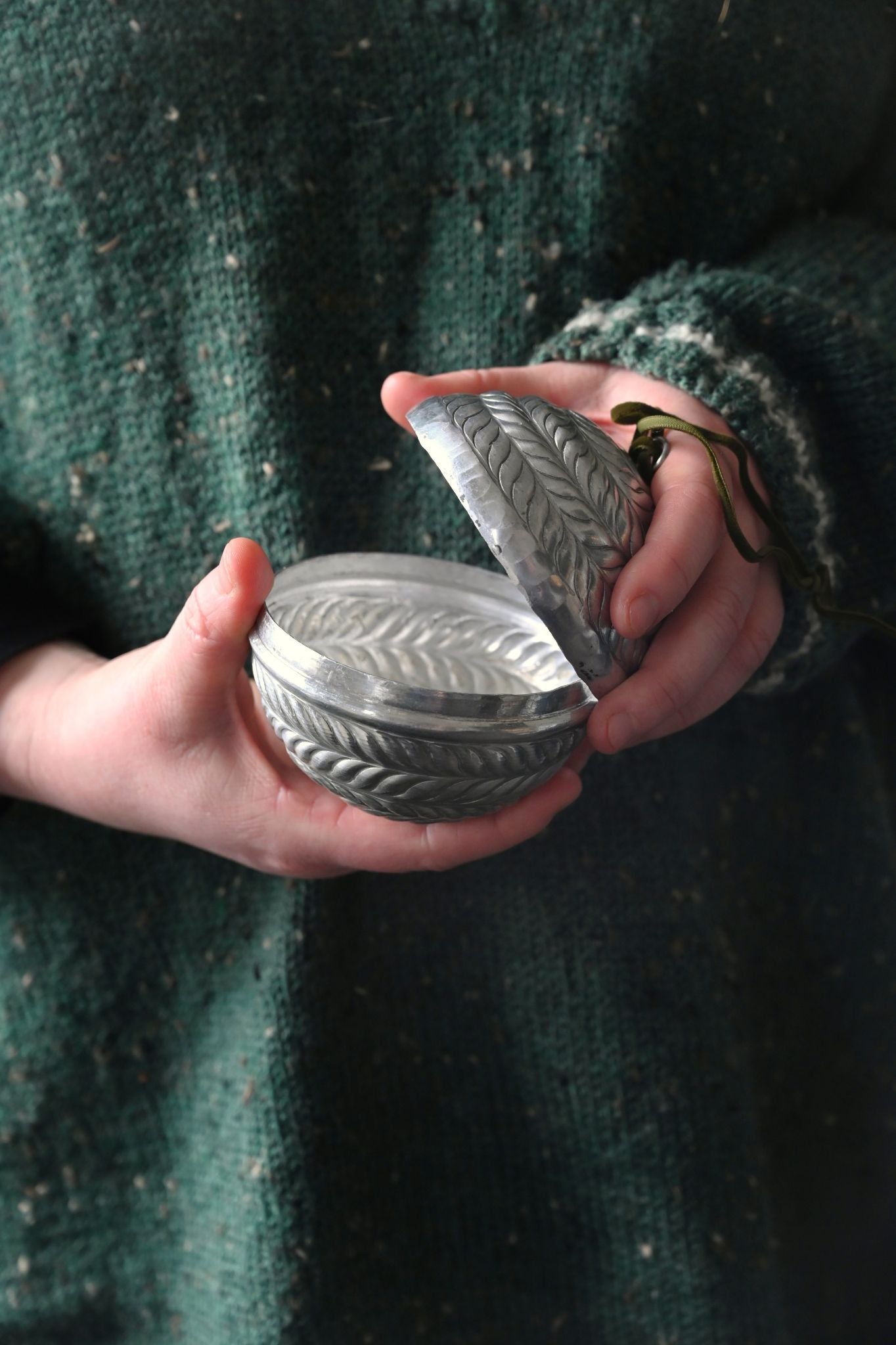 Person holding a silver decorative box with intricate patterns