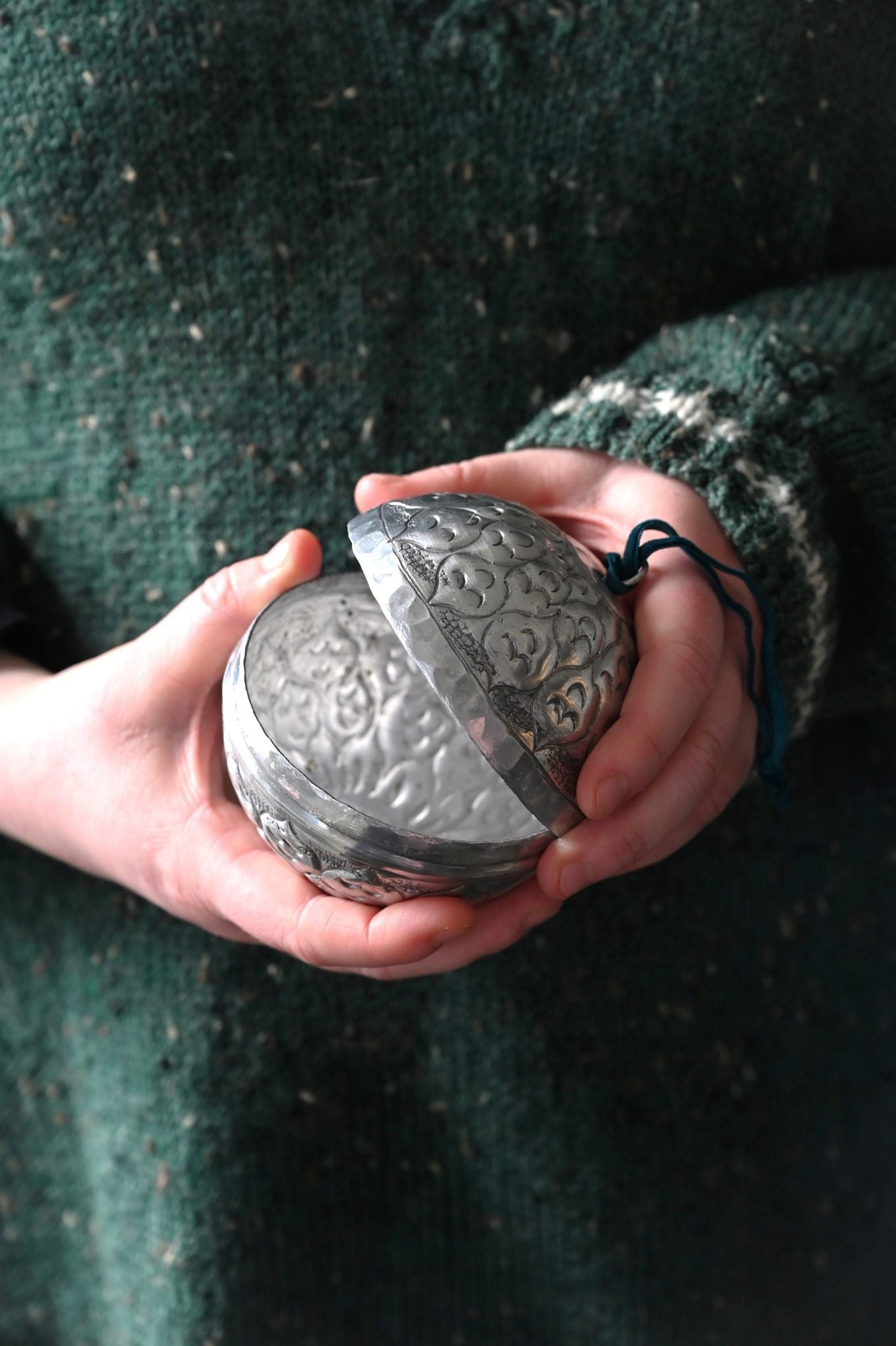 Person holding a metallic, intricately designed round object against a dark background