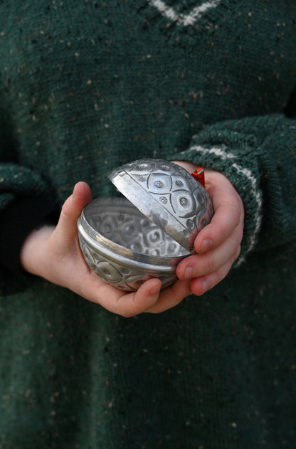 Person holding a silver textured round object against a dark green background