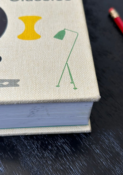 Book with illustrations of a yellow triangle, green lamp, and black circle on a dark surface.