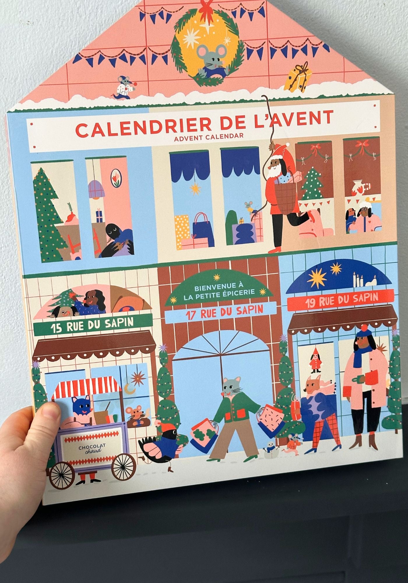 Advent calendar with illustrated scenes of a Christmas town, held by a hand.
