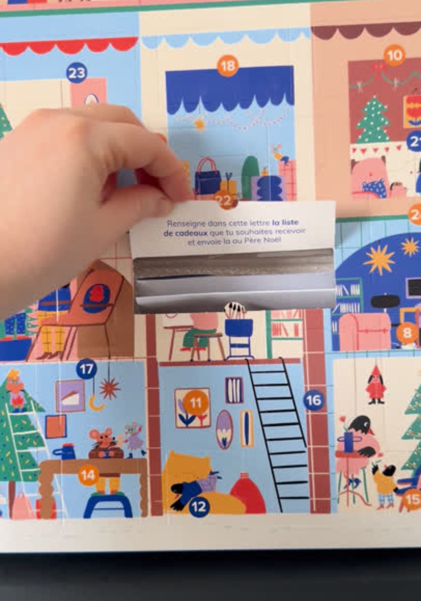Colorful advent calendar with illustrations of a house and people, held open by a hand.