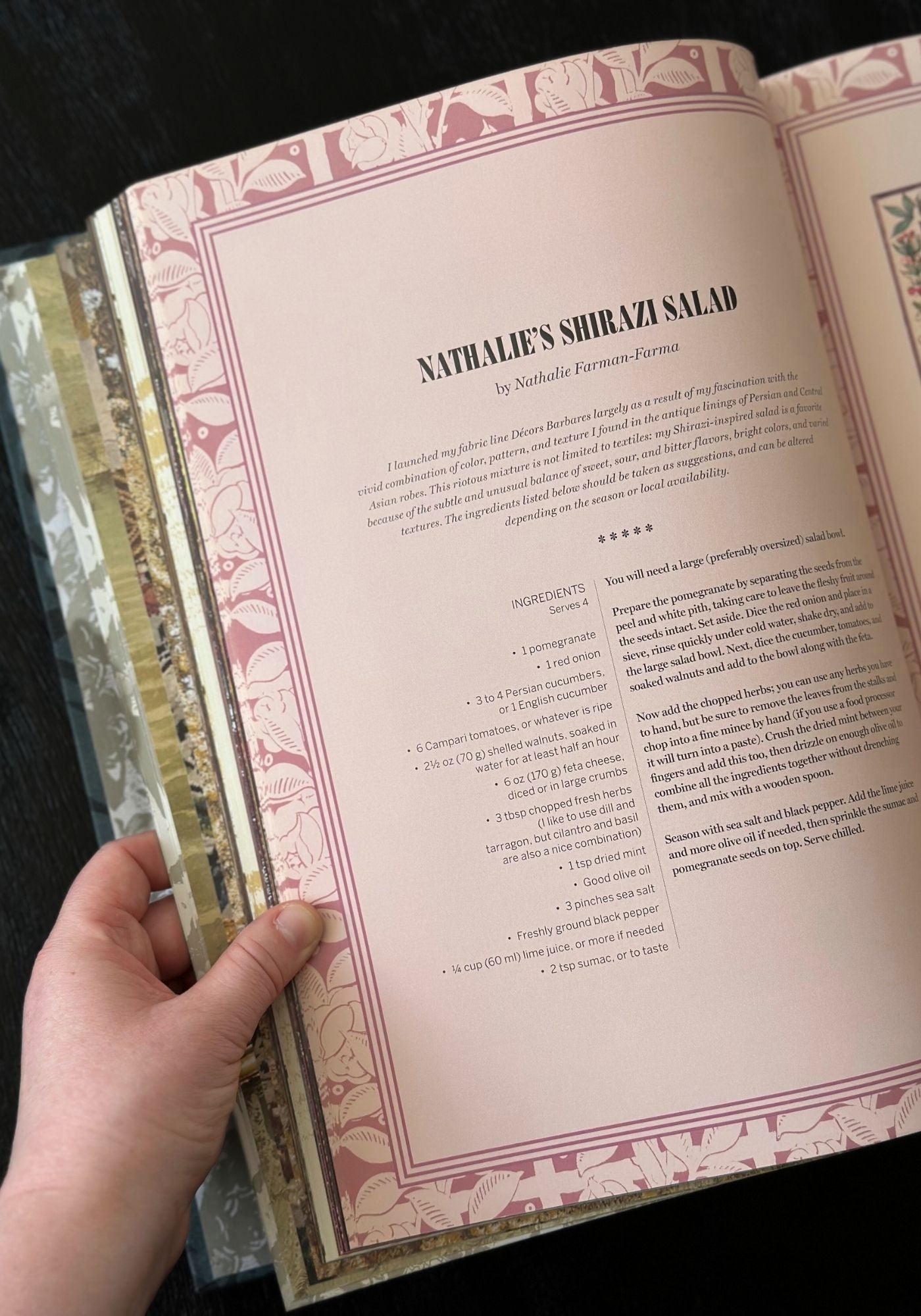 Open book with decorative pages held by a hand, featuring text and ornate design.