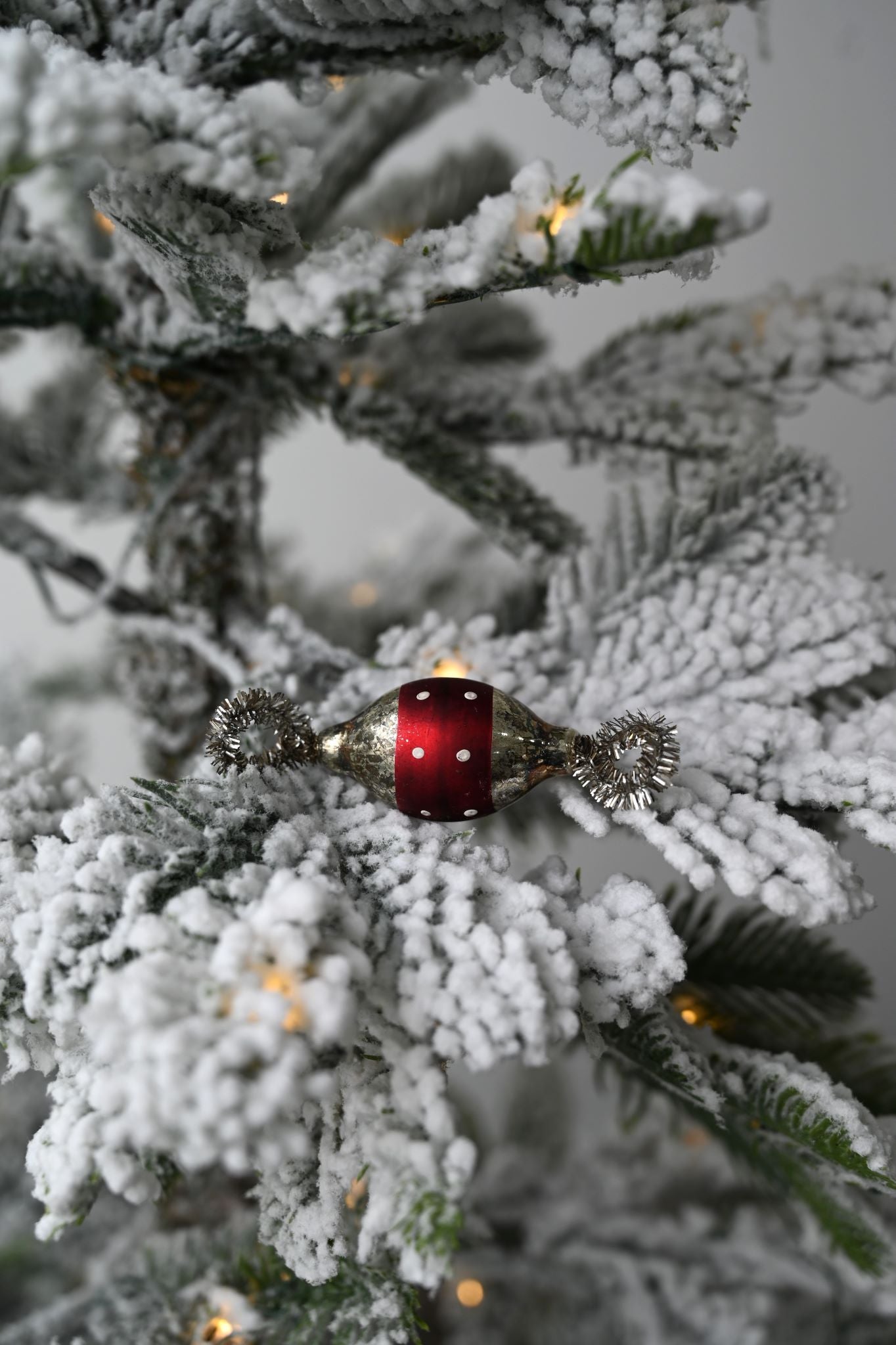 Vintage red polka dot glass sweetie ornament hanging on a snowy Christmas tree.