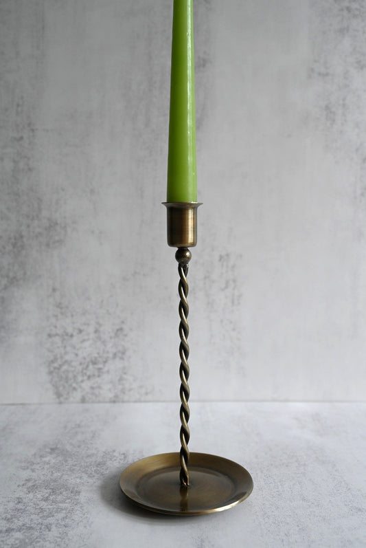 Antique brass candle holders with twisted stems holding colourful tapered candles on a windowsill.
