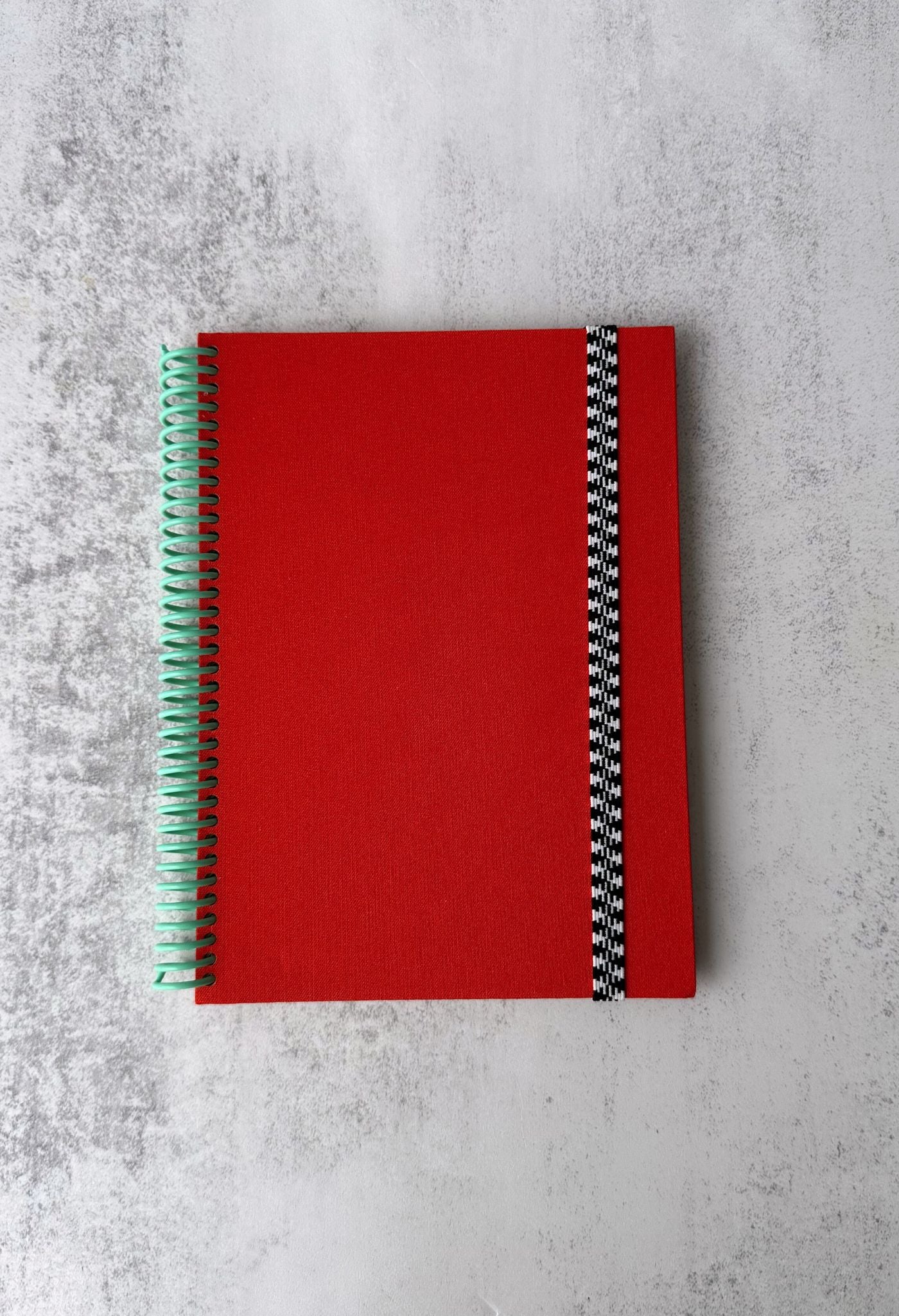 Three stacked A5 canvas notebooks in burgundy, grey, and red with spiral binding.